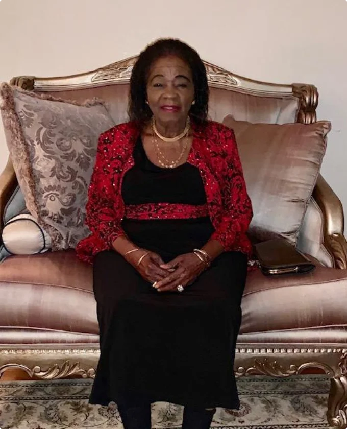 Grace seated on a gilded sofa in a red and black outfit
